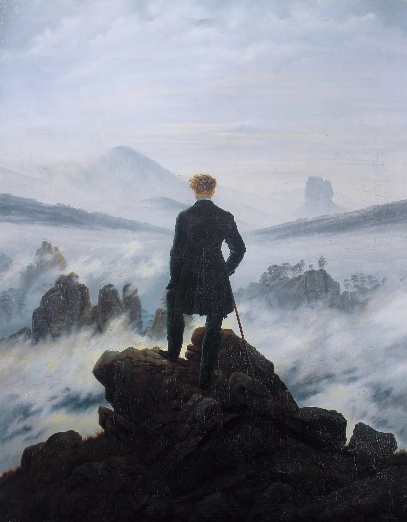 Un homme en manteau vert, appuyé sur une canne, se tient sur un rocher devant des reliefs émergeant du brouillard.